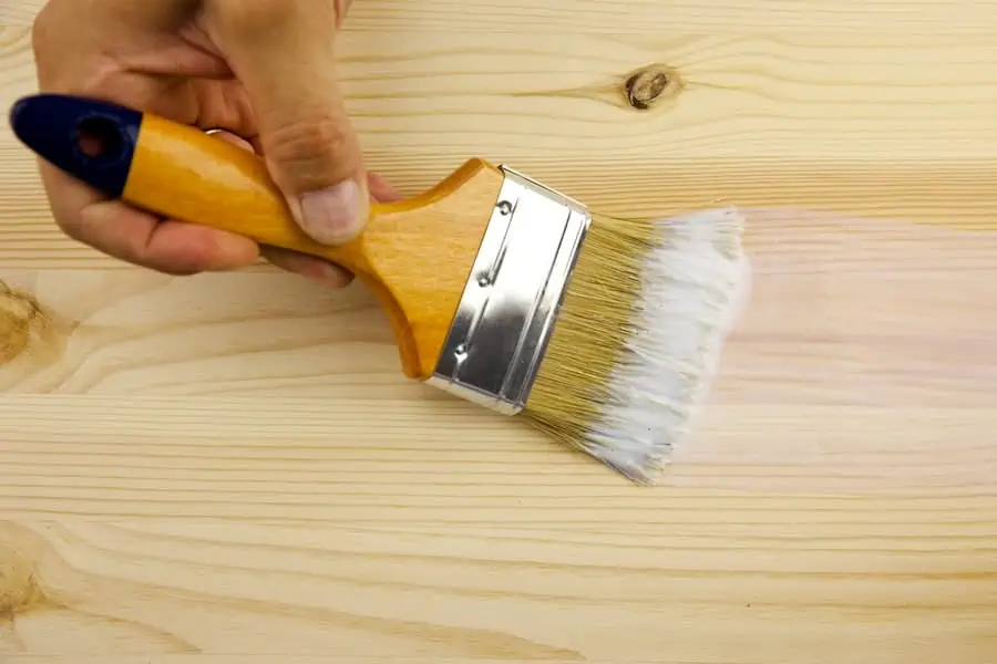 Hand holding a brush to apply polyurethane to a wooden surface.