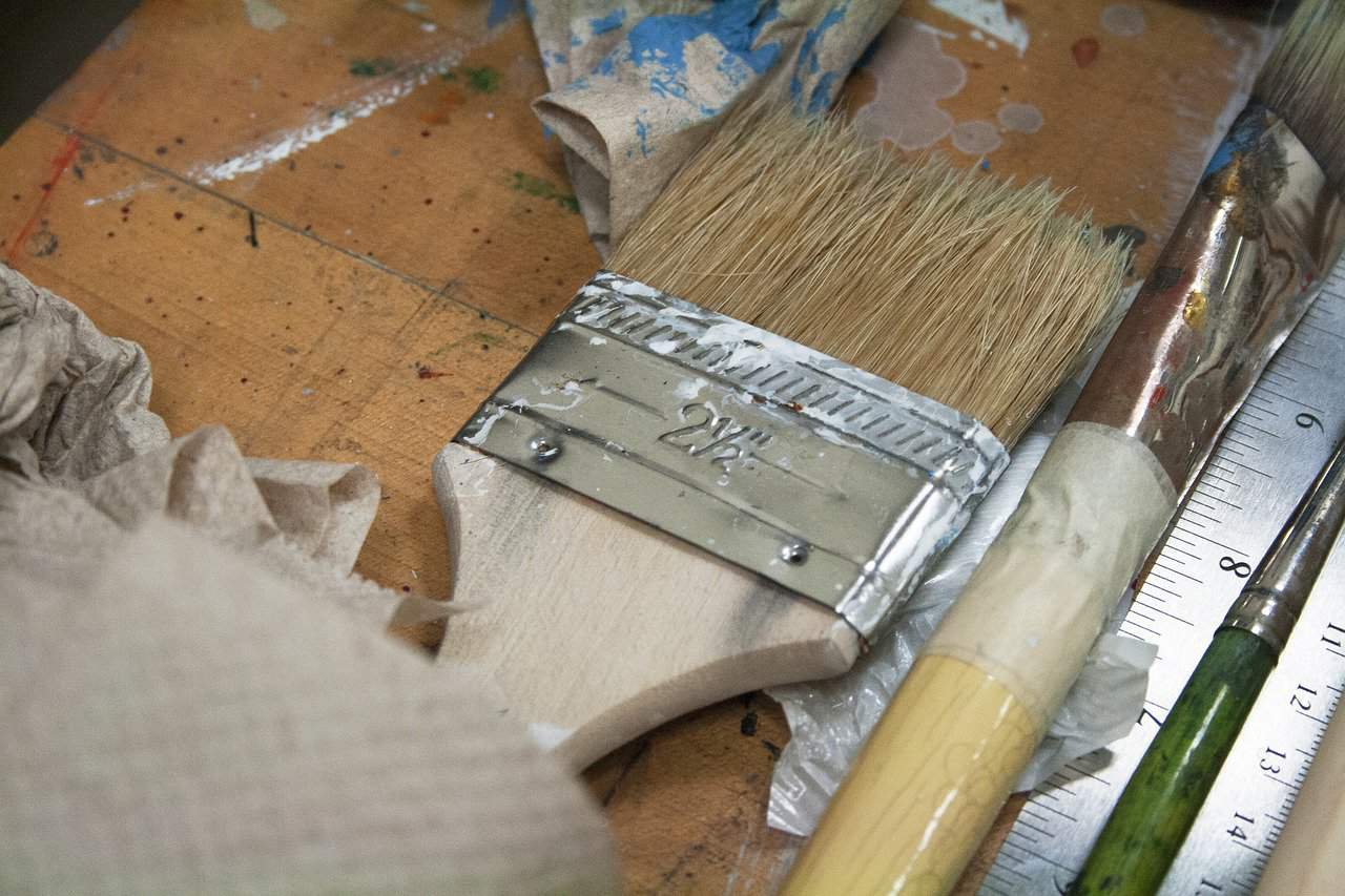 A paintbrush with a white handle is near a silver ruler on top of a brown wooden table