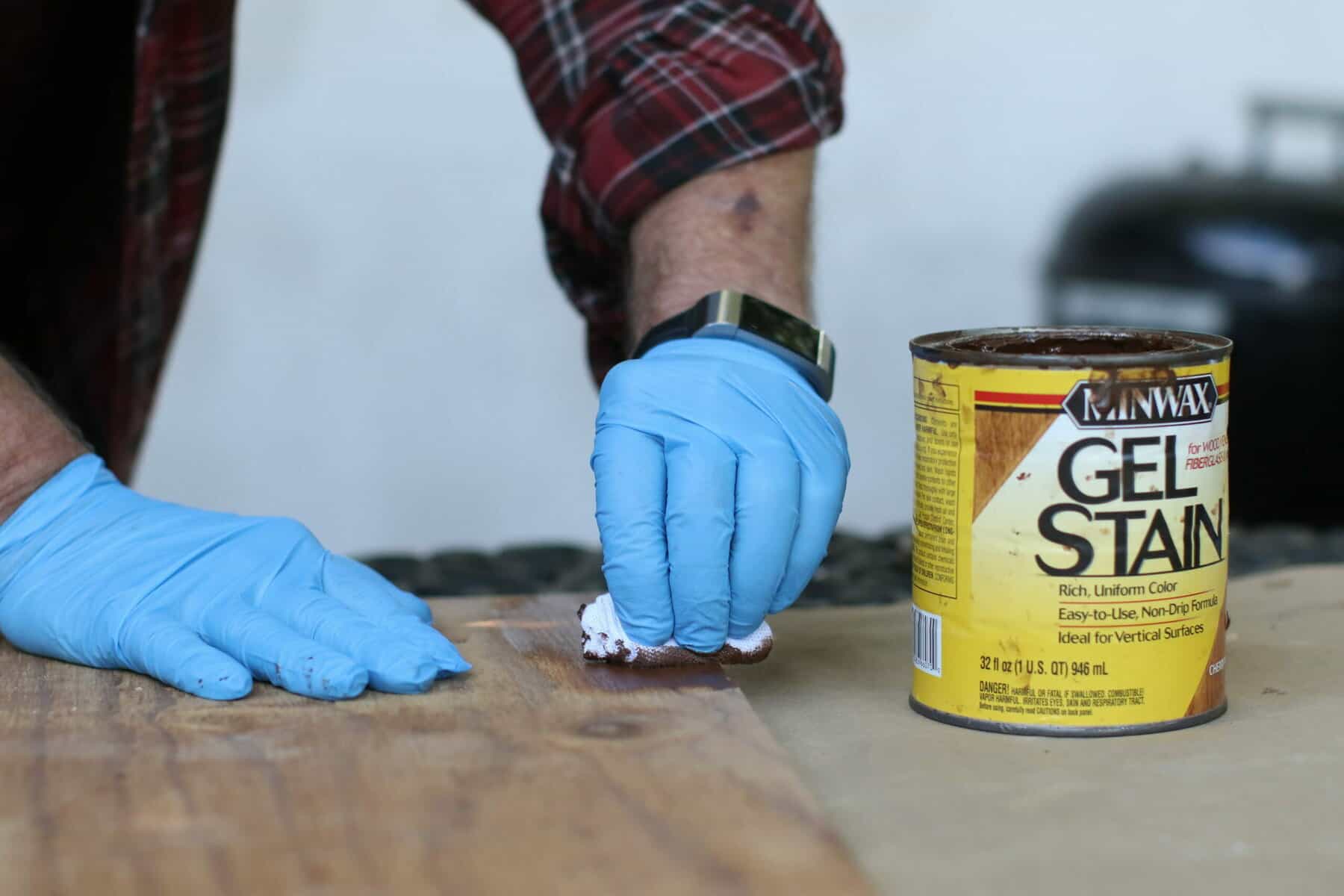 A person wearing blue gloves using a Minwax gel stain to stain a wood