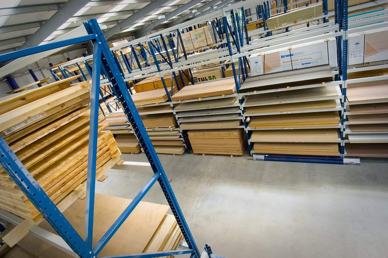 Plywood stacked neatly on blue and white metal shelves on a gray cemented floor inside a well-lit store