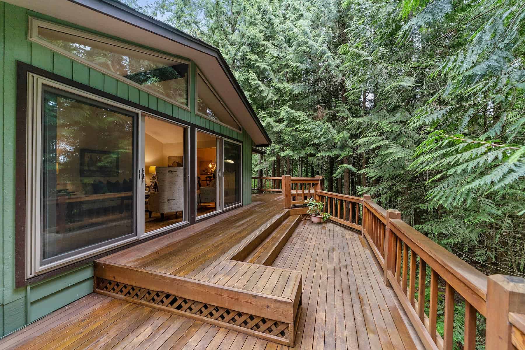A green-painted house with glass doors and a brown wooden deck near tall trees
